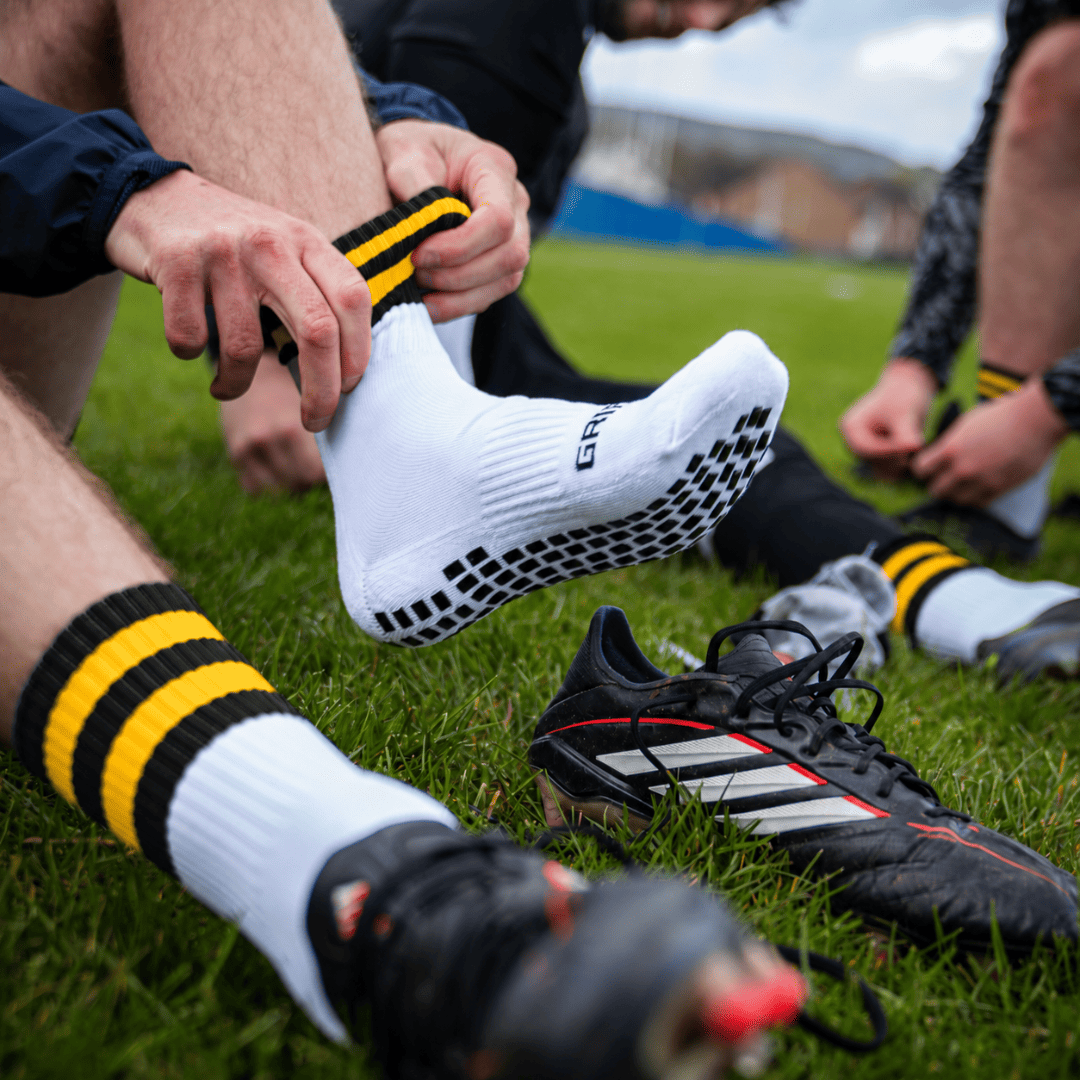 Black and amber GRIPTEC Grip Socks worn with football boots on a pitch
