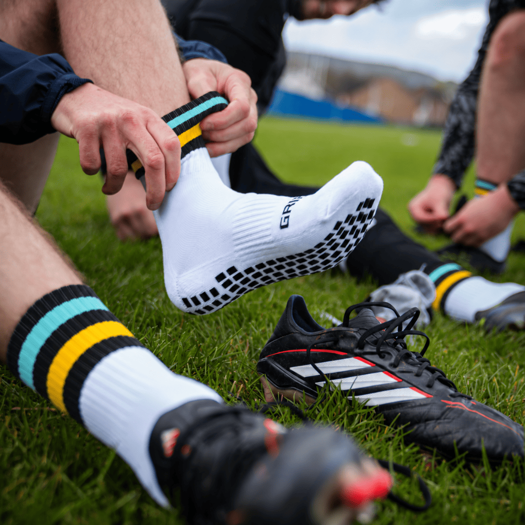 Black, amber and sky blue GRIPTEC Grip Socks worn with football boots on a pitch
