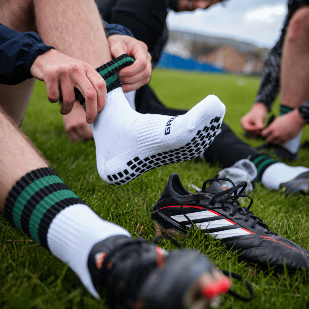 Black and green GRIPTEC Grip Socks worn with football boots on a pitch