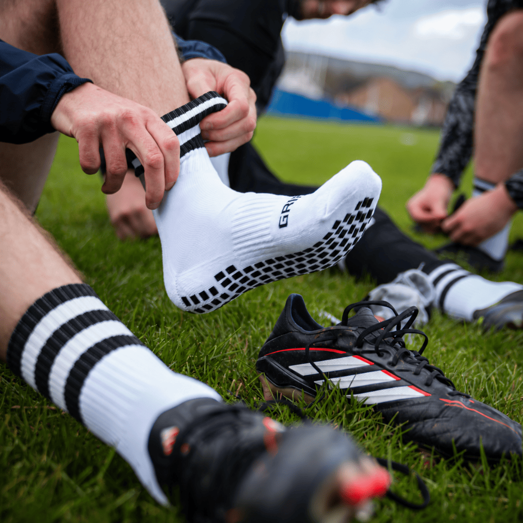 Black and white GRIPTEC Grip Socks worn with football boots on a pitch
