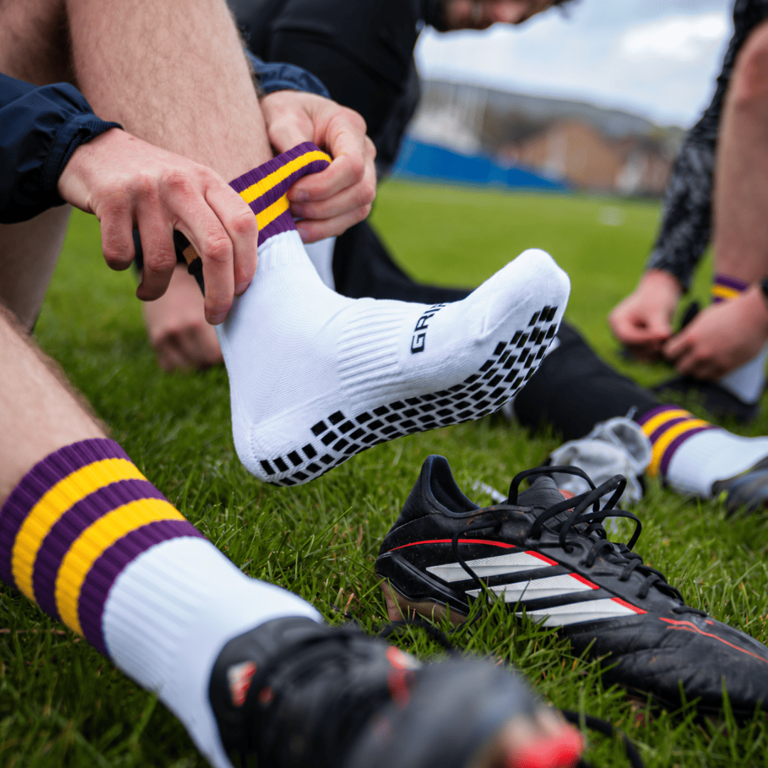 Dark purple and yellow GRIPTEC Grip Socks worn with football boots on a pitch