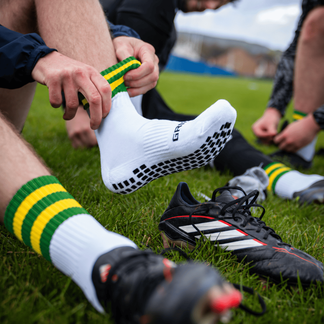 Green and gold GRIPTEC Grip Socks worn with football boots on a pitch