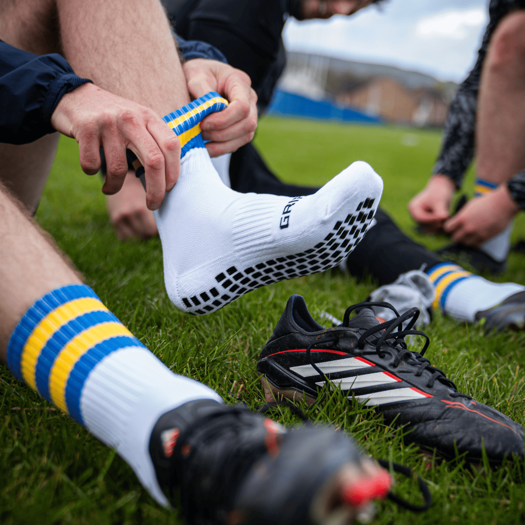 Players pulling on Griptec grip socks pitchside before a match, boots on the grass