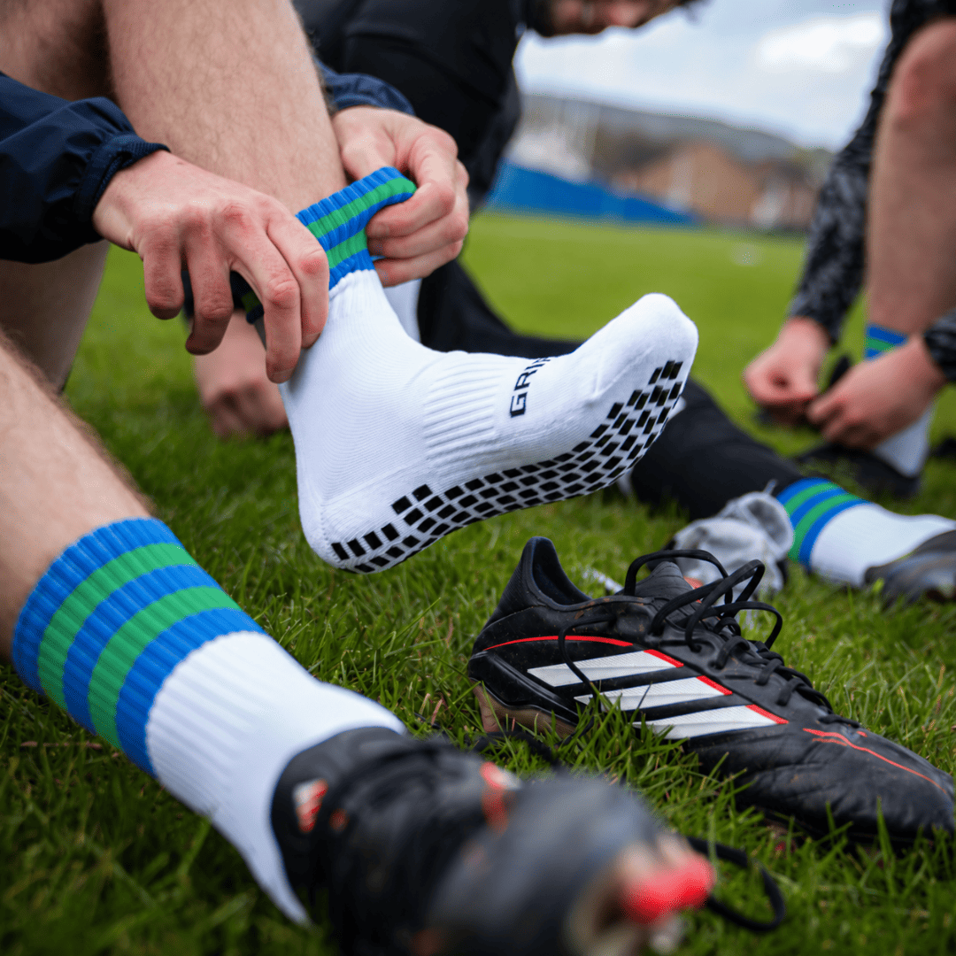 Blue and green GRIPTEC Grip Socks worn with football boots on a pitch