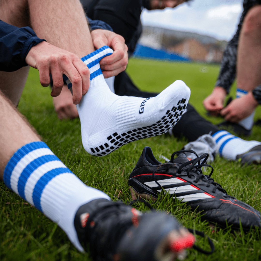 Blue and white GRIPTEC Grip Socks worn with football boots on a pitch