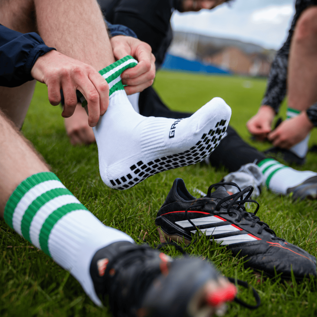 Green and white GRIPTEC Grip Socks worn with football boots on a pitch