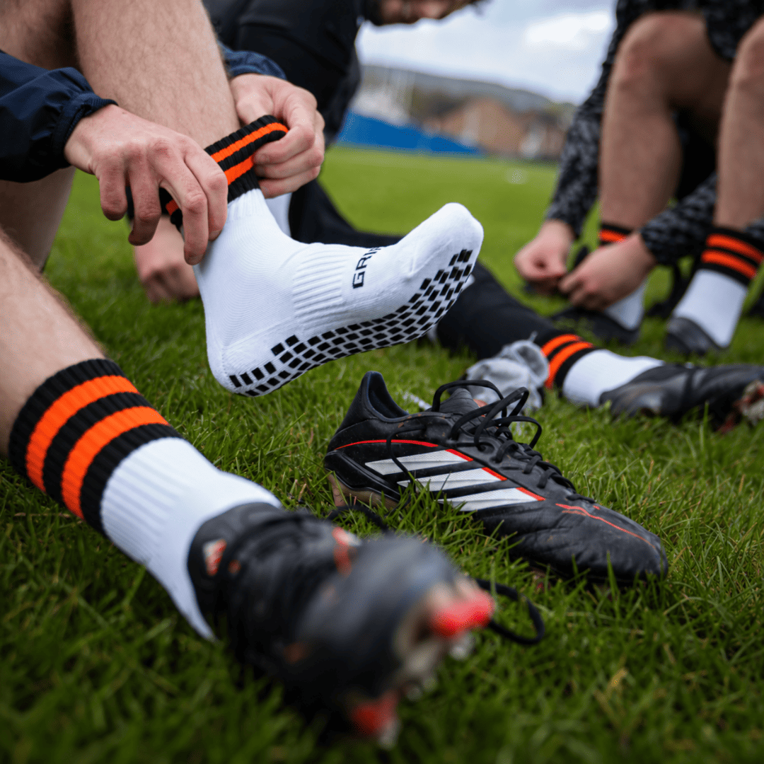 Orange and black GRIPTEC Grip Socks worn with football boots on a pitch