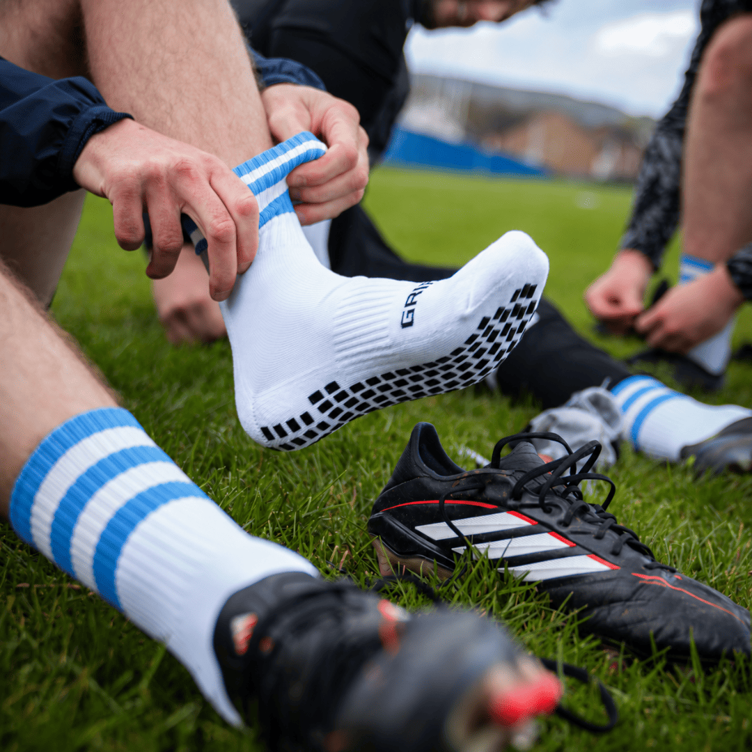 Sky blue and white GRIPTEC Grip Socks worn with football boots on a pitch