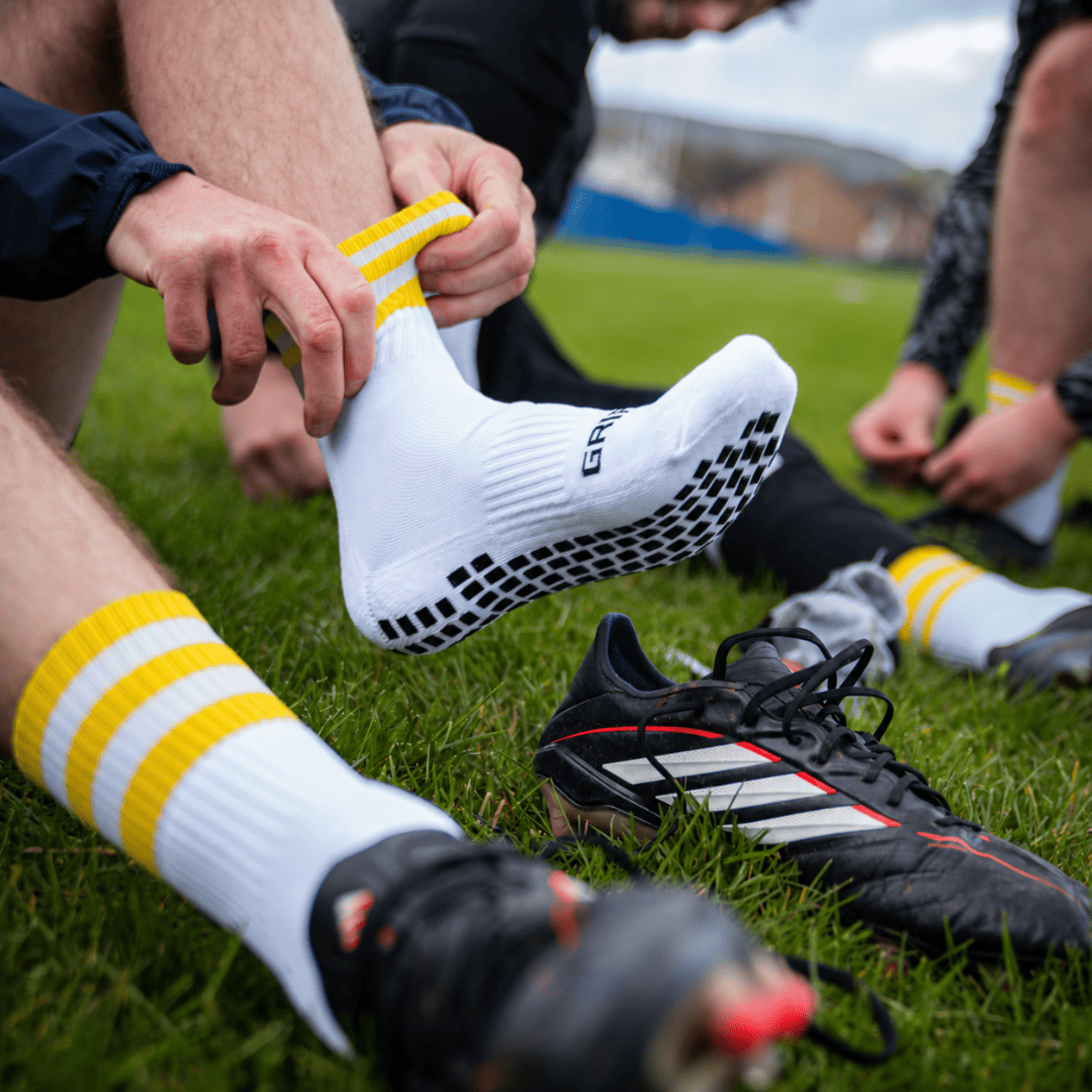 Yellow and white GRIPTEC Grip Socks worn with football boots on a pitch
