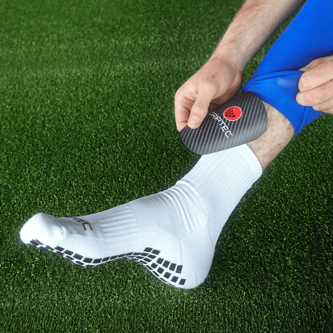 Player pulling a sock sleeve over black GRIPTEC mini shin pads and white grip socks